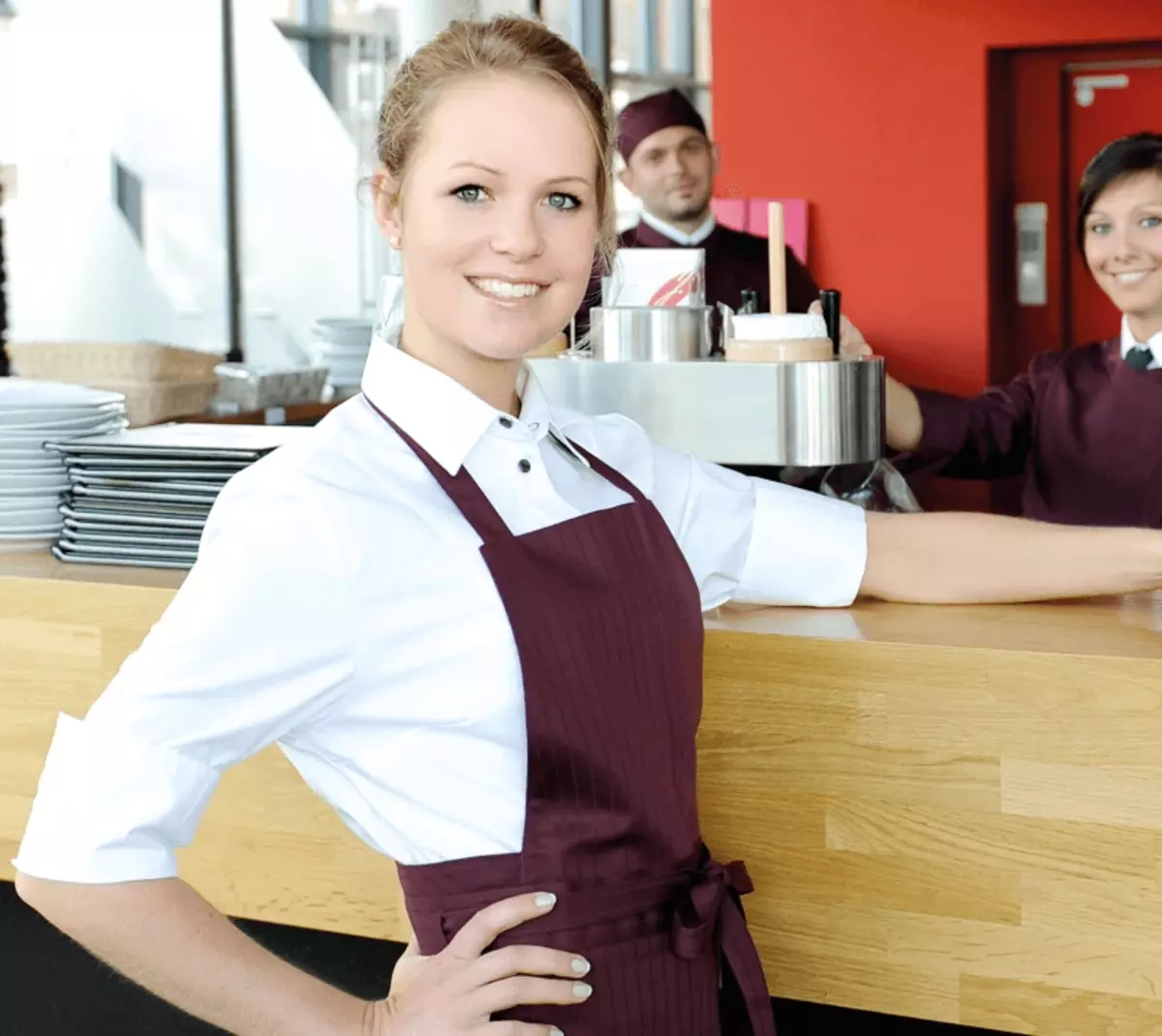 Eine Frau in Schürze. Sie steht an einer Theke und ist als Dienstleisterin im Service aktiv.