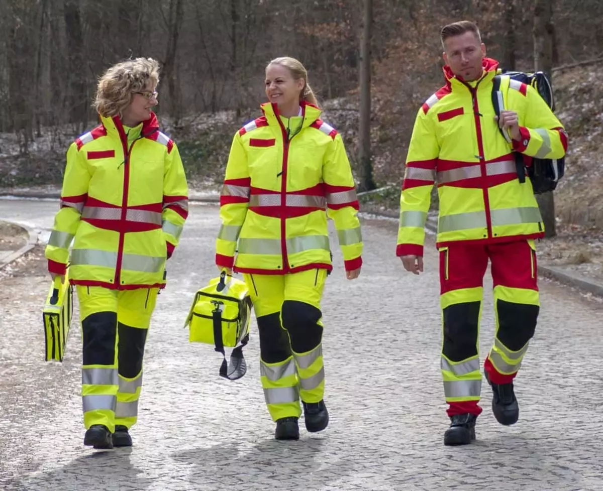 Zwei Frauen und ein Mann in Rettungsbekleidung. Sie laufen eine Straße entlang und lächeln dabei.